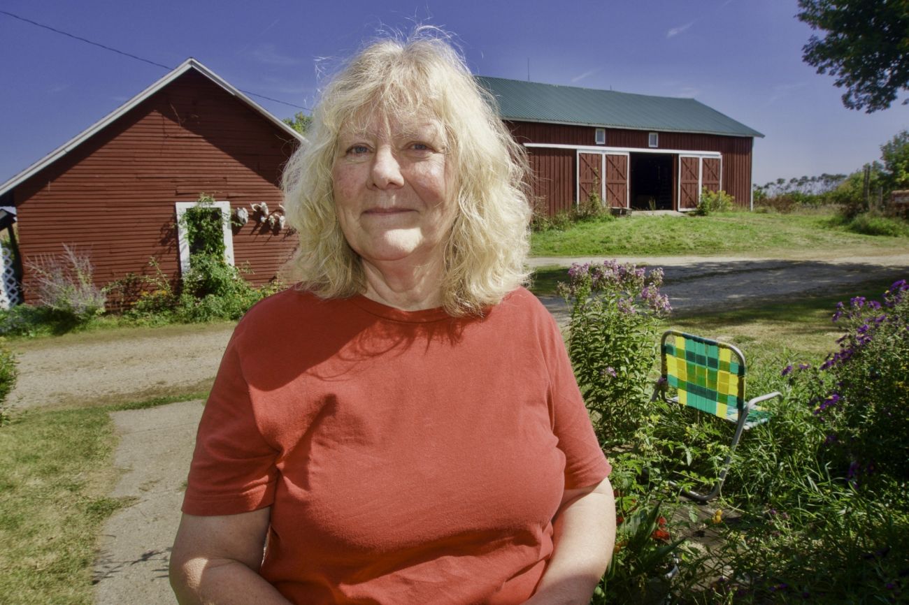 Kathy Morrison, wearing a red t-shirt, poses for a picture in front of a farm