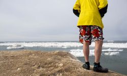 A man in a yellow shirt and shorts. He is about to jump in icy water. 