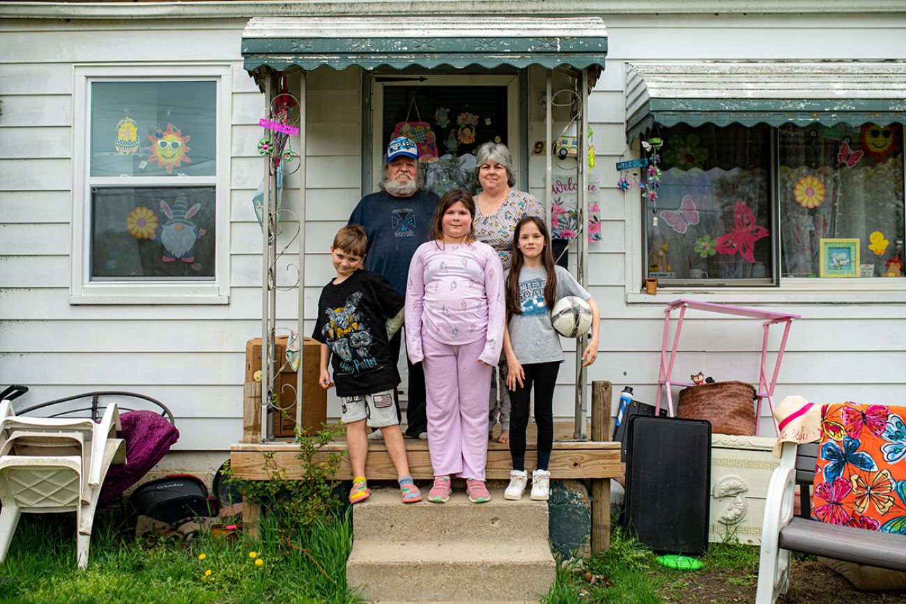 Grandparents with three grandchildren in front of them. They are posing for a picture in front of a house