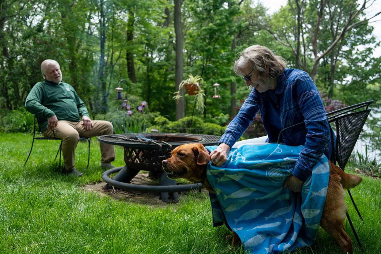 two people sitting outside. the woman is petting a dog