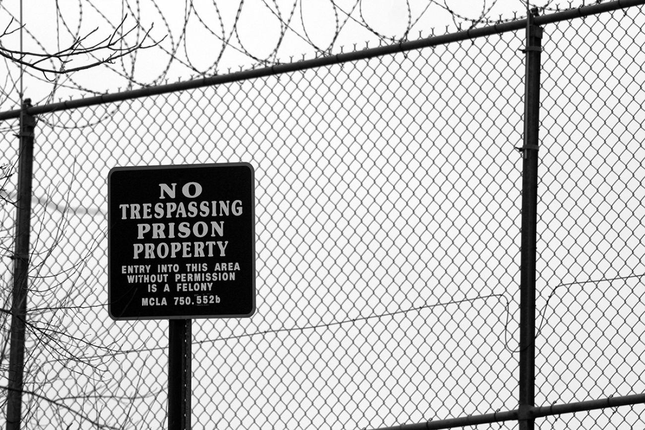  No trespassing sign outside prison fence with barbed wire