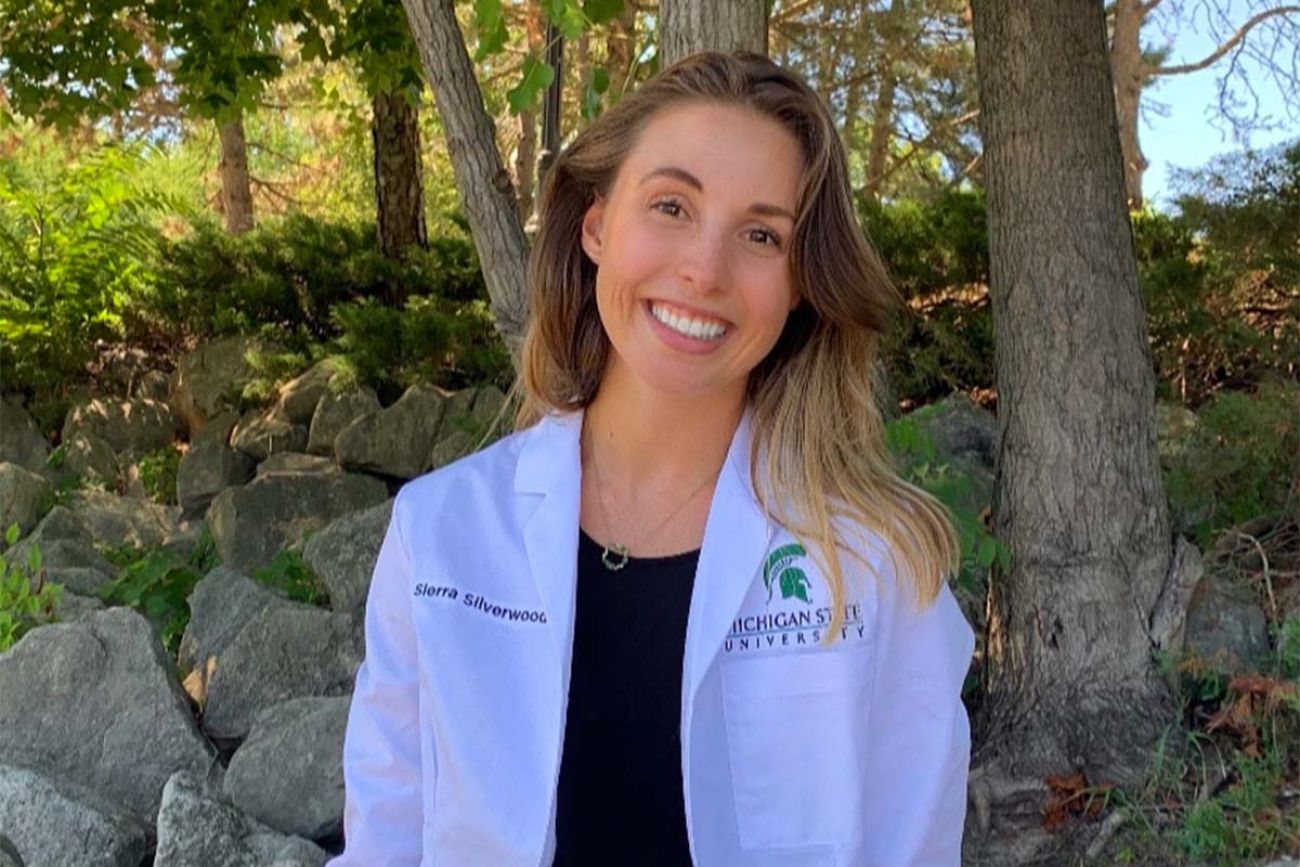 Medical student Sierra Silverwood headshot. She is standing outside and she's wearing a white coat