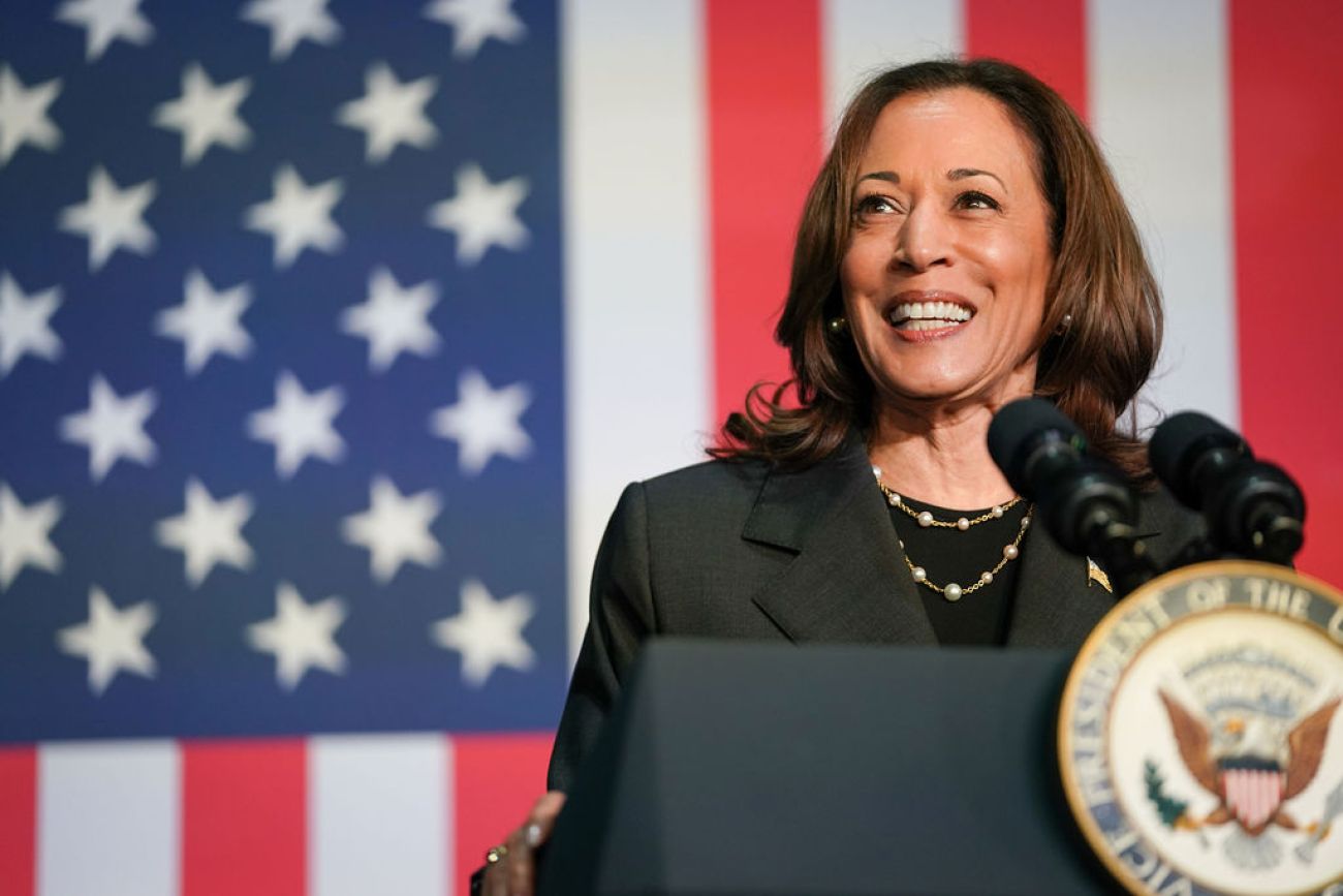 Kamala Harris speaking at a podium, American flag in the background