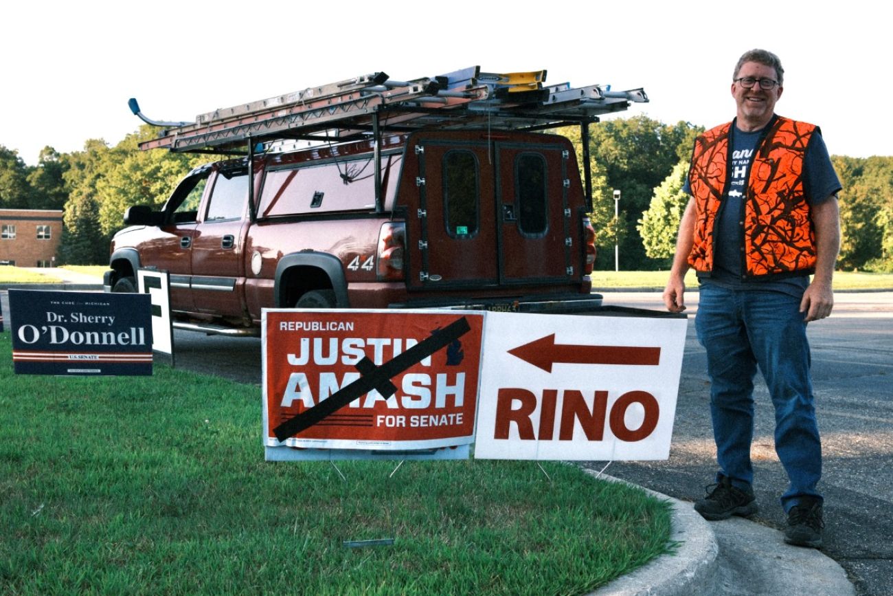 A man standing to a sign that says "Rino" next to a sign for Justin Amash