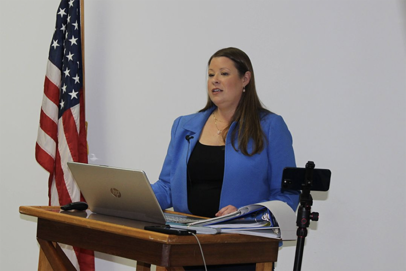 Stefanie Lambert, wearing a blue professional jacket, speaks into a podium