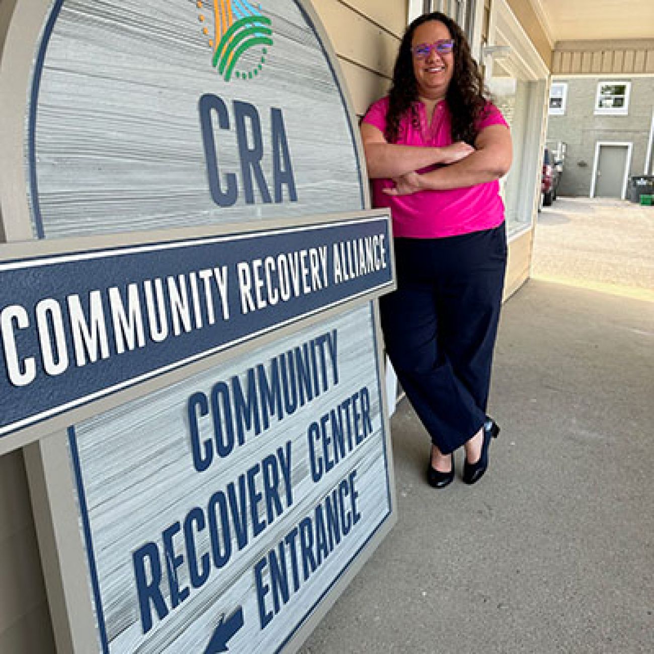 Caitlin Koucky posing photo, next to a sign for the Community Recovery Alliance in Petoskey