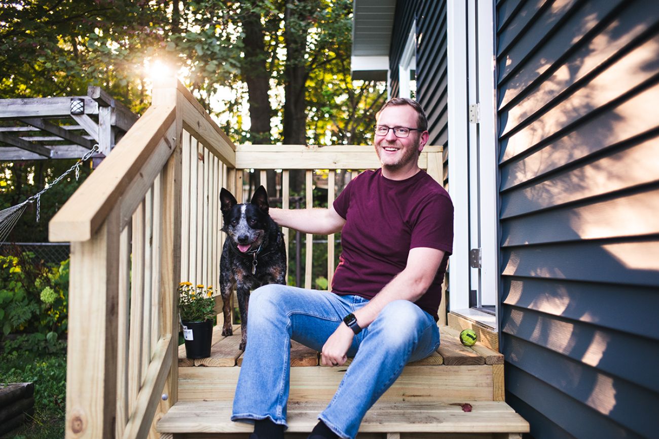 Christopher Germain sits next to his dog. They are sitting on stairs outside the door of a house