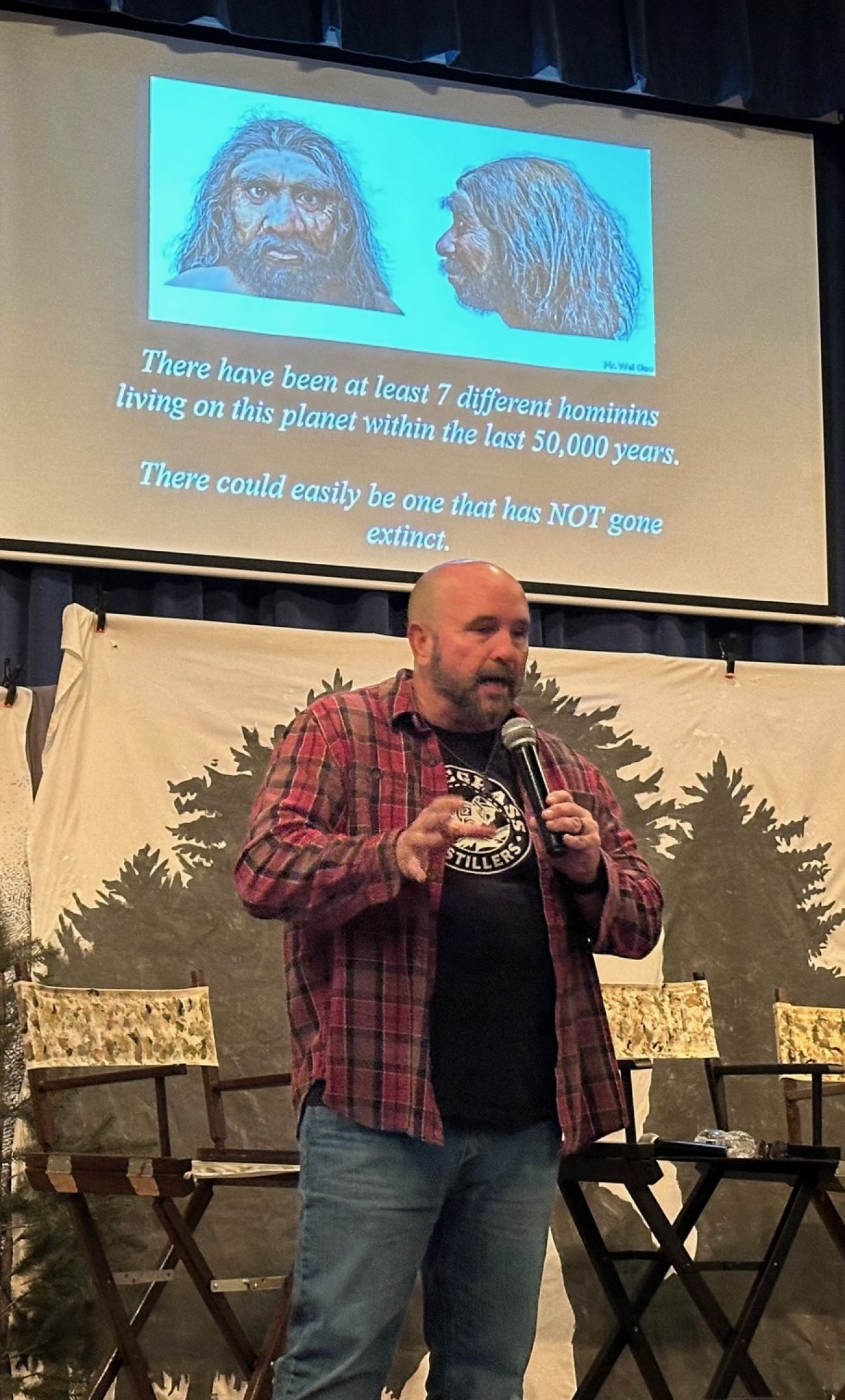 Charlie Raymond stands on a stage. speaking into a microphone