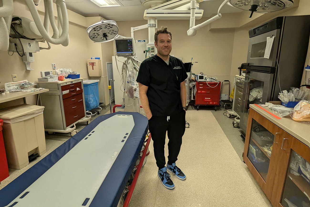 Dr. Bryce Bredell, wearing black scrubs, stands in a room with medical equipment 