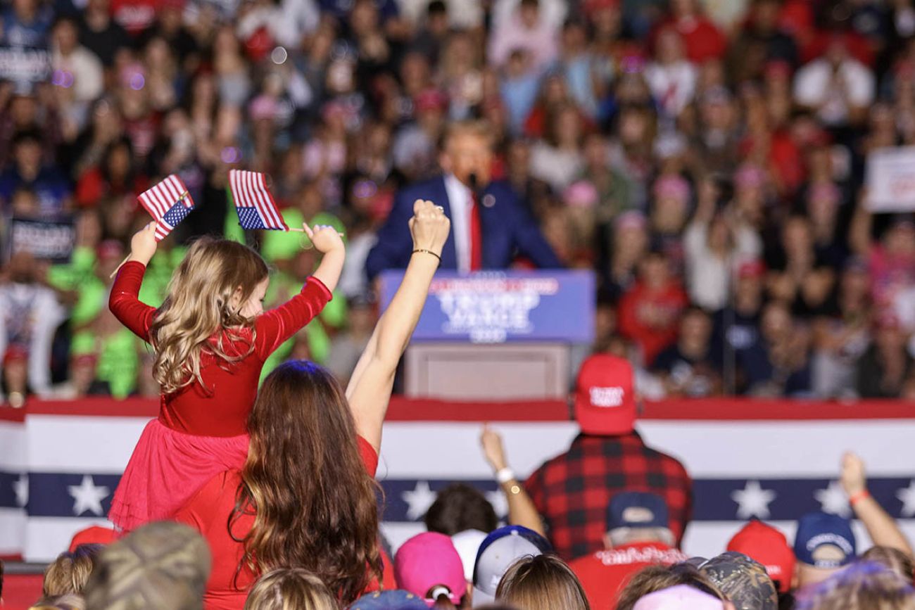 A woman holds up a fist while holding a small girl at a Trump event in Michigan