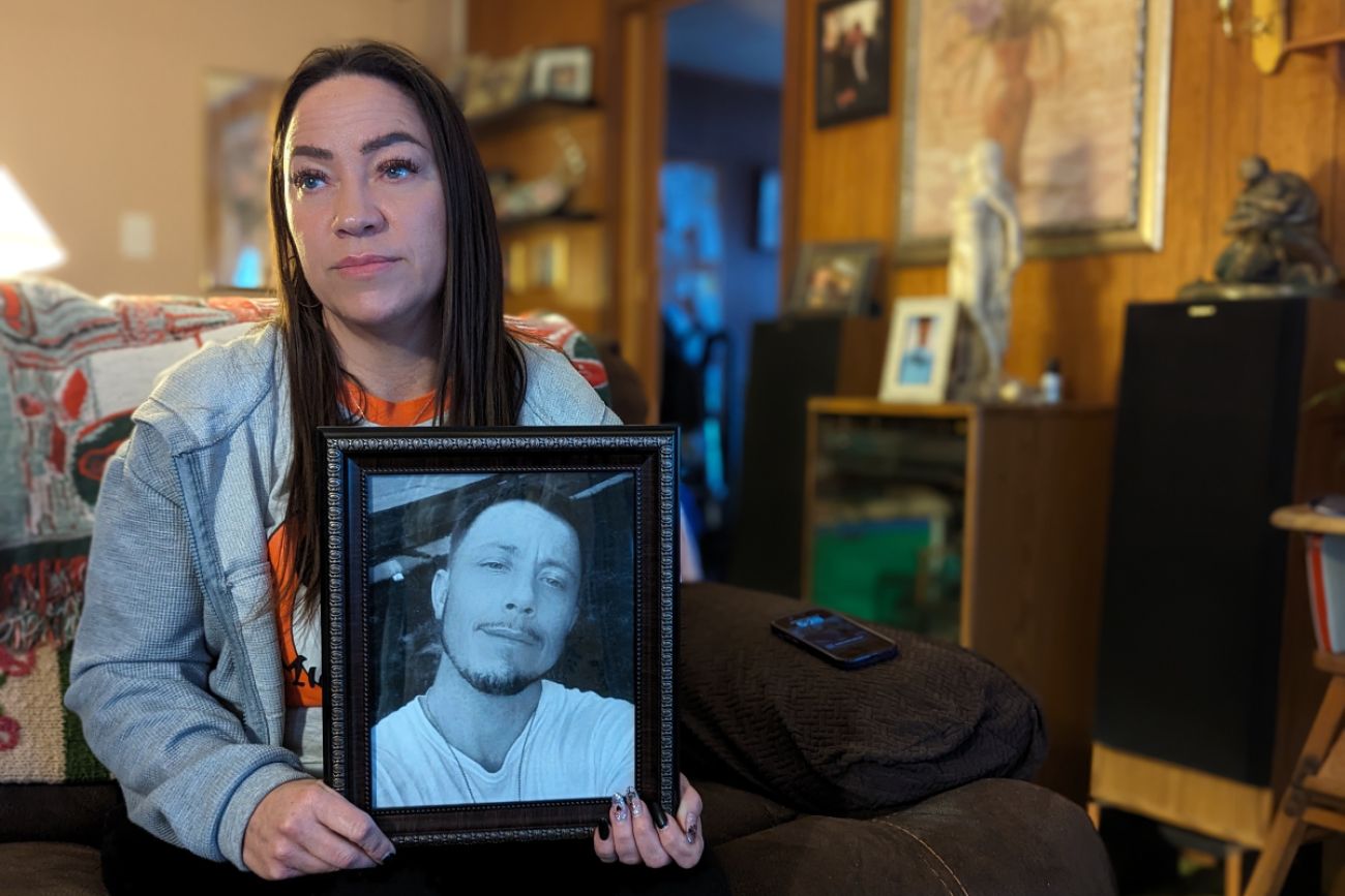 Woman holds a framed photo of a man in black and white