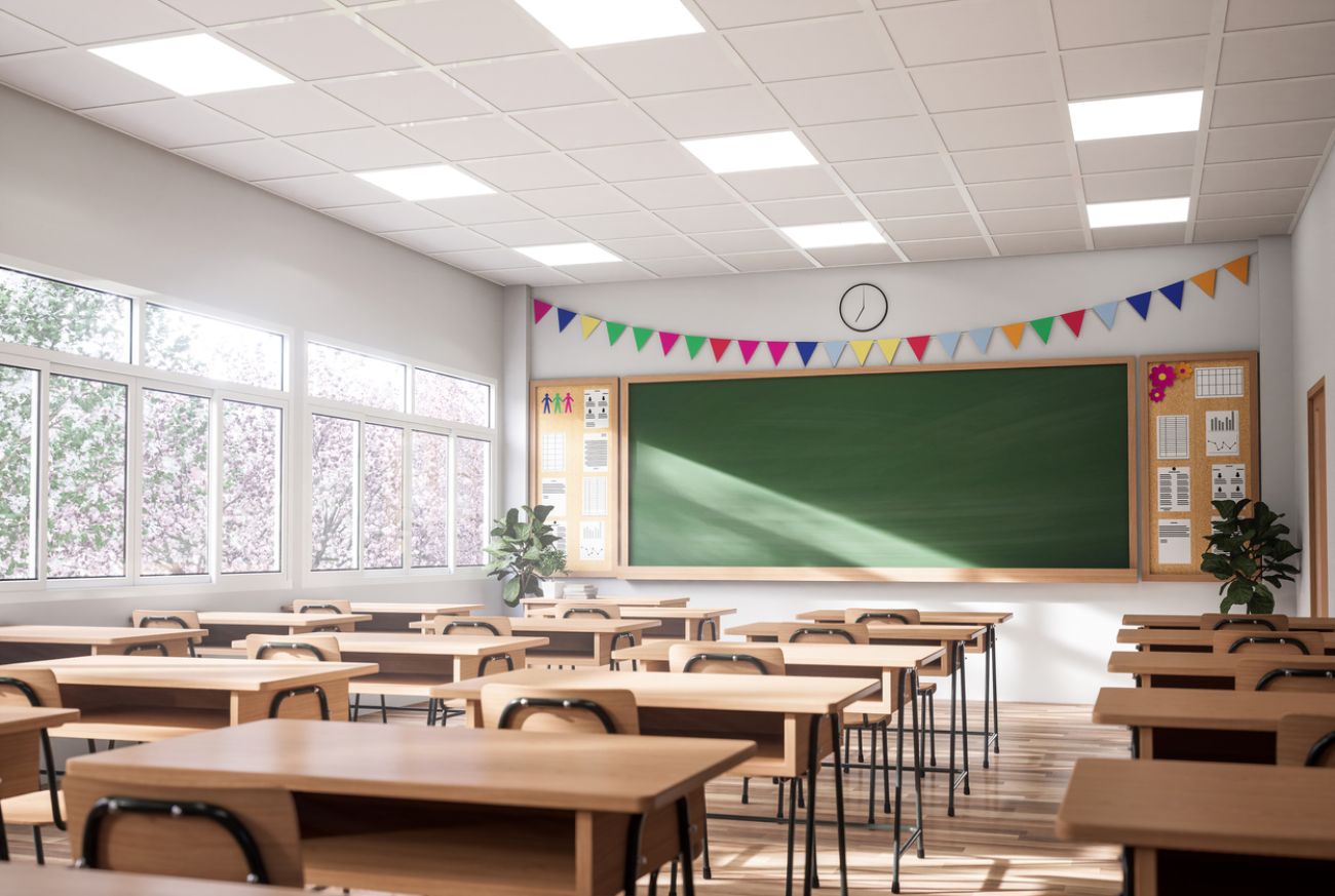 The classroom have white walls and wooden floor, decorated with wooden tables and chairs, large windows overlooking natural views.