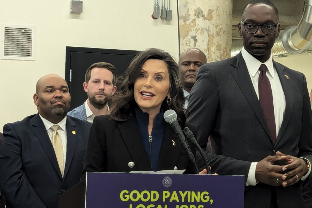 Whitmer stands a podium with people around her