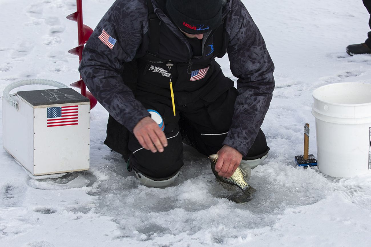 Kevin Kowalski kneels on the icy lake to grab a fish.