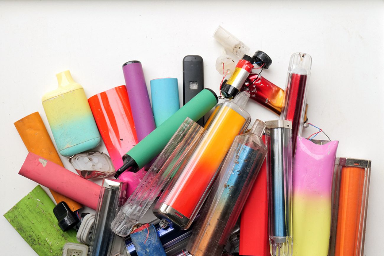 A vibrant collection of discarded electronic cigarette vapes and internal components shot over a white plastic background.