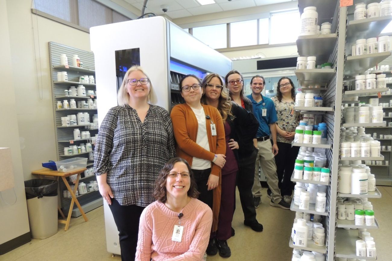 Pharmacy employees pose in front of prescription-filling machine