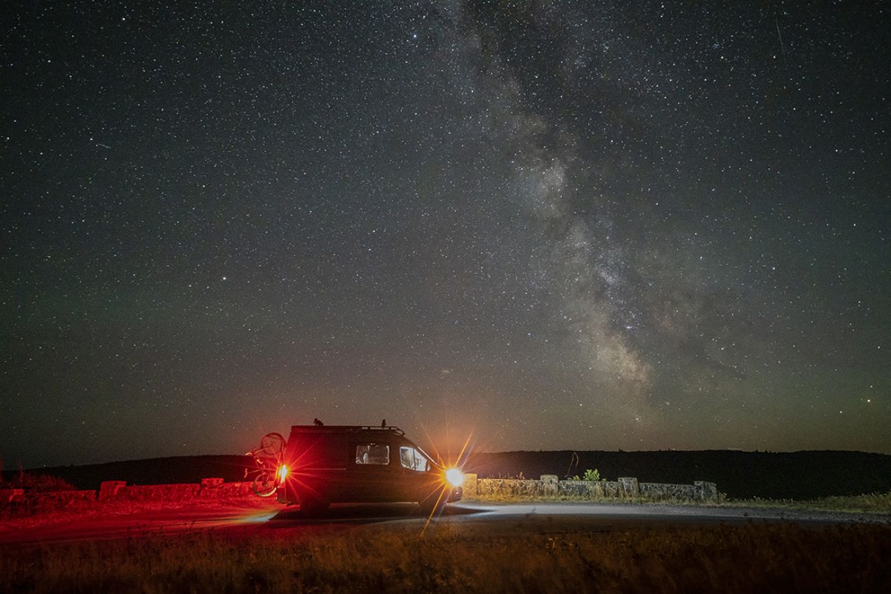 You can see van with red and yellow lights. A bunch of stars can be seen in the night sky. 