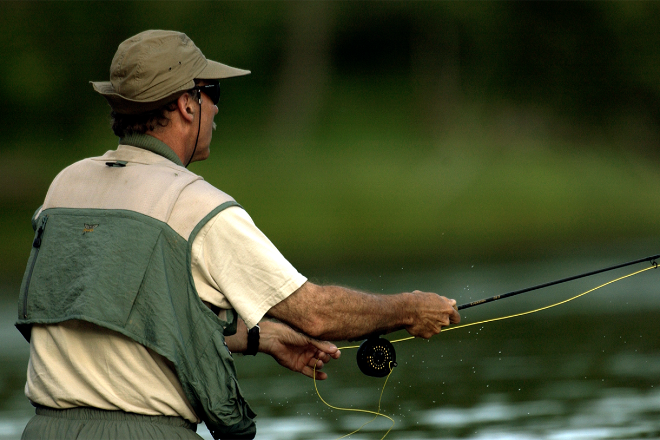 A man fishing. He is wearing green and white clothes.