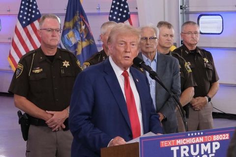 Donald Trump speaking in a microphone, officers are standing behind him