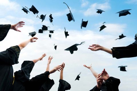 Graduating students hands throwing graduation caps in the air.