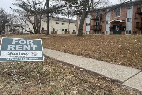 A sign that says "For Rent" in front of an apartment.