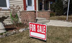 A red and white for sale sign in the front yard of a house