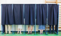 some people voting in at polling booth. They are covered by a black curtain but you can see their feet