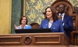 Gov. Gretchen Whitmer speaking into a microphone. Winnie Brinks and Garlin Gilchrist are in the background