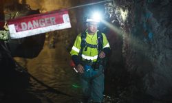 Andy Vaughn, wearing a hard hat with a light on it, walks through a dark mine. You can see a danger sign