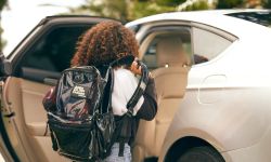 A girl with a backpack goes into a white car