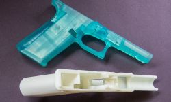 A closeup of 3D printed turquoise and white "Ghost Gun" on a dark background.