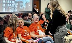 A group of people, many wearing orange t-shirts that says "Save MI Tips" at a committee hearing 