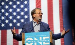 Gary Peters speaking into a microphone, an American flag behind him