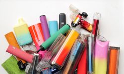 A vibrant collection of discarded electronic cigarette vapes and internal components shot over a white plastic background.