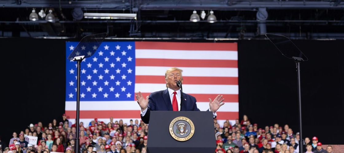 Donald Trump on a stage. People are behind him. 